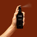 Hand holding Tuttofare Naturally Active Face Mist - 100ml bottle spraying fine mist on warm brown background