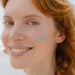 Smiling woman with a dab of Roman Blue Tallow Balm - 70g applied to her cheek in natural light outdoors
